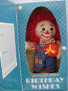 Happy Birthday Raggedy Andy Musical Plush Rag Doll - From the Raggedy Ann Collection. Raggedy Andy Happy Birthday Boxed Gift Doll. Raggedy Andy wears a&nbsp;multi&nbsp;color check shirt and coordinating blue bib overalls.&nbsp; Press his belly and hear "Happy Birthday To You." Comes in a gift box that opens at the front, with spaces to write in to/from. Measures 9" high.&nbsp; Andy is holding a plush gift. safe for ages over 3 