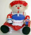 Applause Dakin Limited Edition Raggedy Birthday Bear 85th Anniversary - The Raggedy Bear is dressed in a red print dress with a white sailor color. Peeking out from her her dress is white pantaloons and red and white striped legs.  The bear has red yarn hair.  The cake Raggedy Bear holds reads Happy 85th Birthday and opens to store a small present or treasure.  Raggedy Bear comes with a small Raggedy Ann and Andy rag dolls. 18 inches