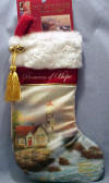 Thomas Kinkade 'Beacon of Hope' Limited Edition Christmas Stocking - The top of the stocking is white faux fur, then a red velvety stripe with the name of the stocking embroidered in white, and the rest is a SOFT brushed material. There is gold trim embroidered between the colors and textures. The Kinkade logo is embroidered with shiny gold threads onto the toe of the stocking. There is a red velvety hanger attached at the top to use to hang the stocking by the chimney with care! There is a gold tassel with a jingle bell attached to it. 15 inches