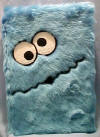 Sesame Street Plush Covered Cookie Monster Journal - the journal is really a hard covered book except it has a plush covering over it to look just like Cookie Monster's blue furry body with his face on the front. the inside of the journal fratures Cookie monster peeking over the top each page.  9 inches by 6 1/2 inches by 1 1/4 inches