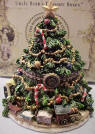 Front view of Boyds Uncle Beans Treasure Box Kringles Christmas Tree - (Introduced in Fall 2003 and has been retired) This magnificent Christmas tree treasure box-decked with baubles, beads, candy canes, a star topper, and a choo choo train around the base--opens to reveal a special holiday message on the inside lid; a cookie and milk tray for Santa; and, underneath, Frazier, an elf mouse wrapped up in colored lights. Quote: "Merry Christmas to all and to all a good night!"